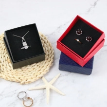 Necklace and ring boxes in black, red, and blue on a marble surface with starfish