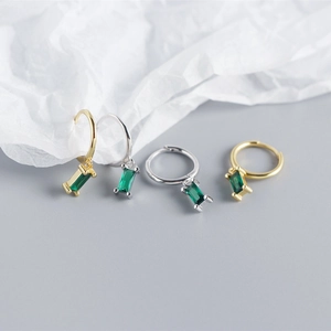 Close-up of minimalist gold and silver hoop earrings with emerald green zircon pendants