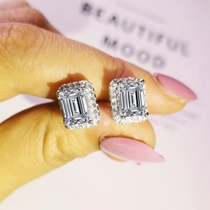 Detail of emerald cut stud earrings with halo diamonds shown on hand model