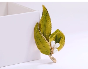 Detail of green enamel leaf brooch with white pearls and gold trim on white background