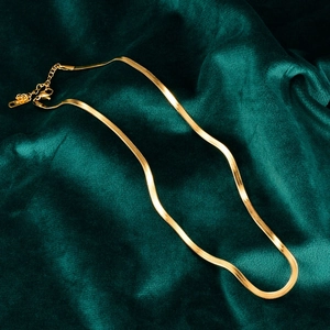 Close-up of golden snake bone chain necklace with lobster clasp on green velvet