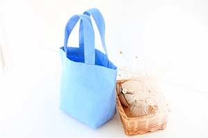 Detail shot of a light blue canvas tote bag on a cozy table with a wicker basket