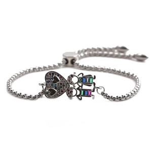 Détail d'un bracelet ajustable argenté avec cœur en zircon et breloques garçon et fille