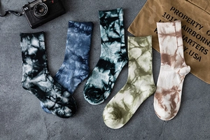 Flat lay of five tie-dye mid-calf cotton socks in various colors on a concrete surface