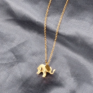 Golden elephant pendant necklace with a polished finish on a dark textured background