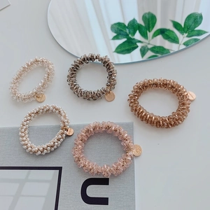 Flat lay of five beaded elastic hair ties with gold charms on a minimalist background