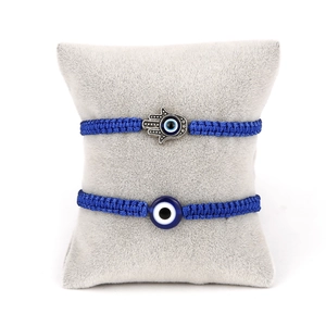 Detail of blue woven Hamsa Hand and Evil Eye charm bracelets on a grey display pillow