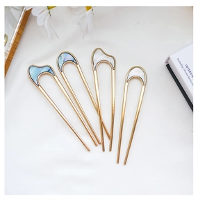 Detailed macro view of four golden U-shaped hairpins with elegant shell inlay on white cloth