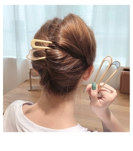 Detail of a gold U-shaped metal hair pin with marble texture held by a hand