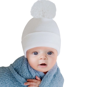 Macro detail of a soft white newborn baby knit beanie featuring a fluffy pom-pom.