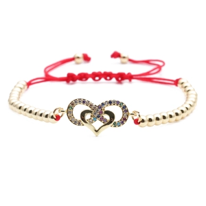 Detail of red braided cord bracelet with gold heart and infinity charm set with zircons