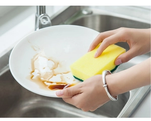 Dual-sided sponge cleaning a ceramic plate over a stainless steel kitchen sink