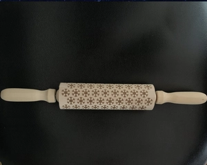 Detailed close-up of wooden rolling pin featuring intricate engraved snowflake patterns