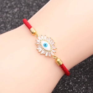 Detail of red braided cord bracelet with gold evil eye charm and clear zircons on wrist