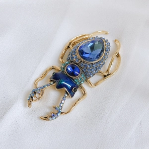 Detailed macro view of an ornate beetle brooch with blue rhinestones and gold metal finish