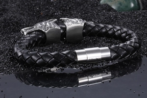 Detail of woven black leather bracelet with engraved silver wolf heads and magnetic clasp