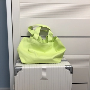 Detail van de ruime neon groene canvas draagtas geplaatst op een witte reiskoffer