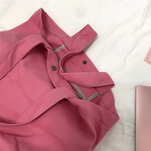 Detail van roze canvas tas met grove textuur en bronzen magnetische knoopsluiting