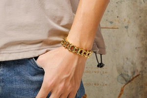 Detail showing a gold-plated stainless steel curb chain bracelet worn on a man's wrist