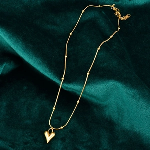 Close-up of golden 18K gold-plated heart necklace with bead chain on green velvet