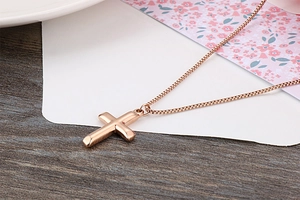 Close-up of minimalist rose gold cross necklace on box chain with mirror finish