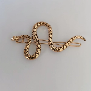 Detailed close-up of golden snake hairpin with black cross patterns on white background