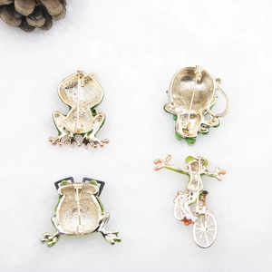 Detail view of four golden frog brooches showing secure back pins on white plush background