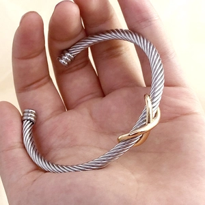 Detail view of silver twisted cable bracelet featuring a golden X-shaped decorative clasp