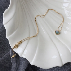 Detail of 18K gold heart pendant with iridescent shell inlay on a white shell tray