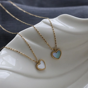 Macro shot of 18K gold plated heart shell pendants on white wave ceramic stand
