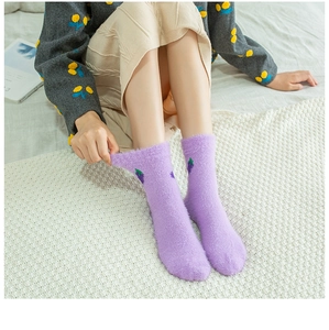 Close-up of soft purple coral fleece socks with grape embroidery on white knit carpet