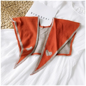 Detail of knitted orange shawl scarf featuring grey heart jacquard and ribbed edges