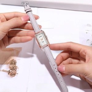 Detailed close-up of a rectangular rose gold quartz watch with a slim gray leather strap