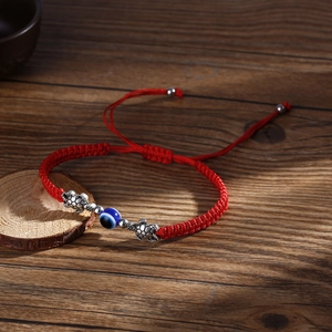 Red braided Evil Eye bracelet with silver turtle charms on a vintage wooden surface