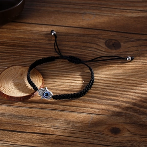 Handmade black woven Evil Eye Hamsa Hand bracelet on wooden background with adjustable cord