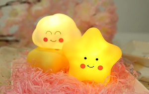 Close-up of glowing star and cloud night lights with smiles in a decorative pink nest