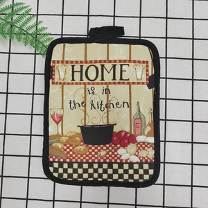 Close-up of a beige cotton oven mat with a black hanging loop on a checkered tablecloth