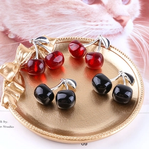 Sweet cherry pendant accessories in red and black colors displayed on a gold tray