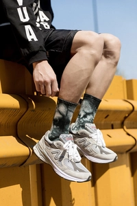 Detailed view of green tie-dye mid-tube socks worn with grey suede lifestyle sneakers