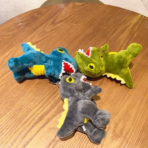 Cute plush dinosaur keychains in blue, green, and grey on a wooden background