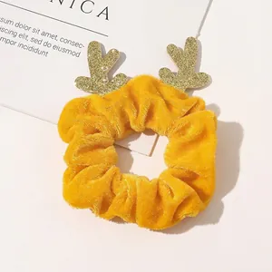 Detail of yellow velvet Christmas scrunchie with golden glitter reindeer antlers on white background