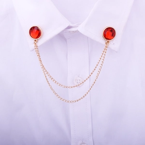 Detail of a gold collar pin featuring red faceted gems and double tassel chains on a shirt