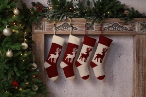 Detail of four knitted Christmas stockings with reindeer patterns on a wooden fireplace