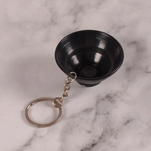 Close-up of a glossy black funnel-shaped keychain pendant on a grey marble background