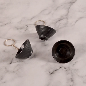 Close-up of black miniature plastic bowl keychain with fine spiral texture on marble background