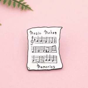 Détail d'un pin's émaillé en forme de partition avec texte Music Makes Memories