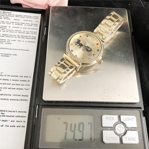 Macro shot of gold couple's watch with horse logo weighing 74.97g on a digital scale