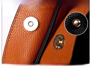 Detailed close-up of metallic magnetic buckle on orange and black lychee leather bag