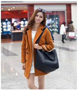 Woman in brown coat carrying a large black leather tote bag in a bright modern setting