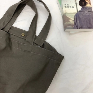 Detailopname van canvas tas met bronzen drukknoop en witte contraststiksels
